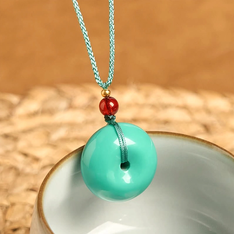 Overhead view of turquoise peace buckle tibetan necklace with gold spacer bead and red decorative bead on ceramic bowl background