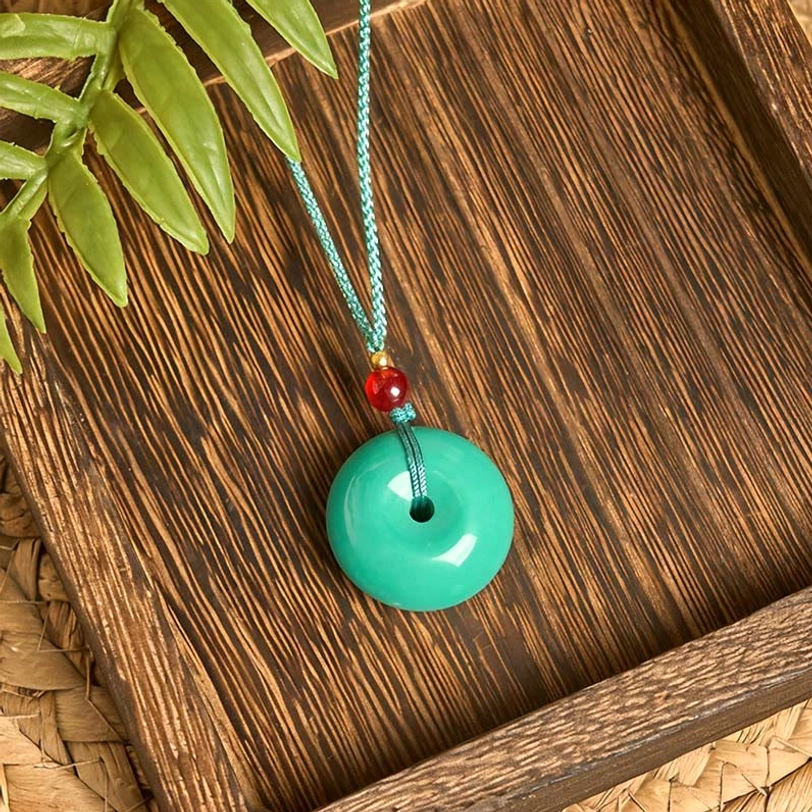 Side angle view of turquoise peace buckle pendant necklace with natural green foliage on wooden plank background
