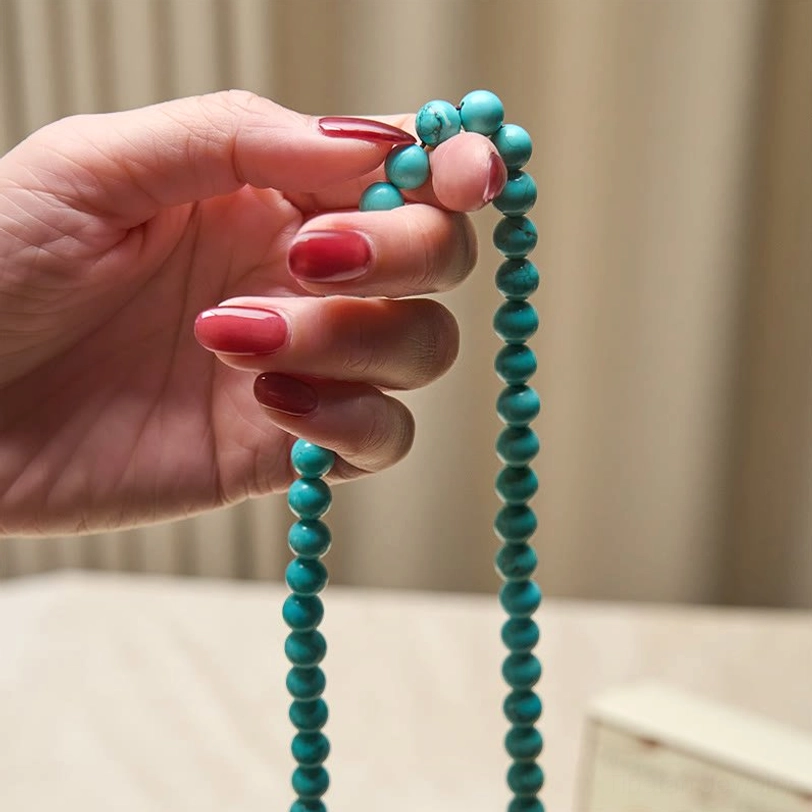 Hand-held turquoise mala beads necklace with natural stone texture and brown tassel - held by hand with red nail polish