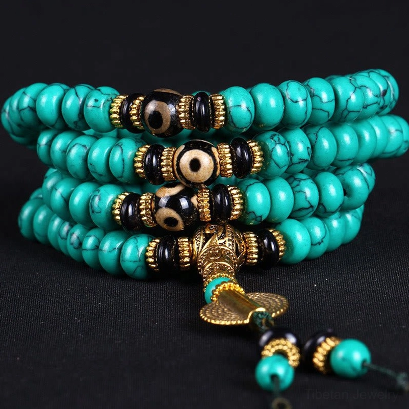 Layered turquoise mala bracelet with black dzi spacer beads and gold pendants on dark background