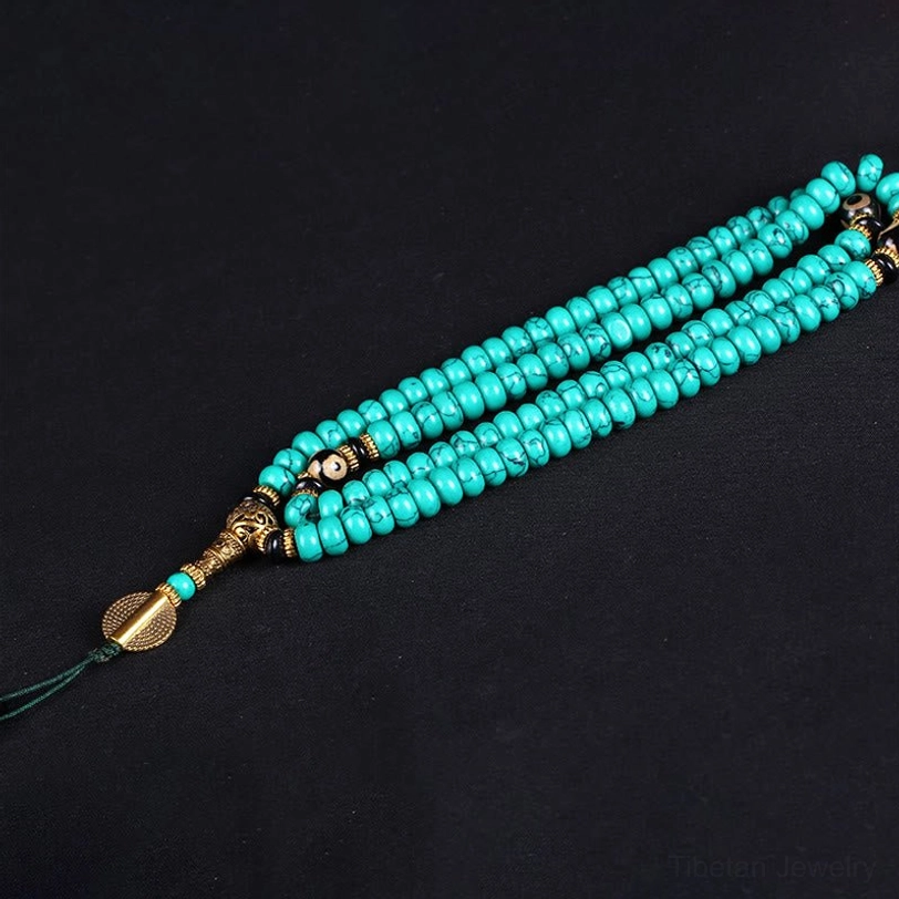 Long turquoise mala strand with small beads and gold tone end fittings on dark background