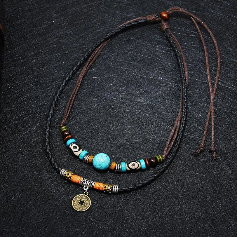 Overhead view of turquoise ethnic layered necklace with two-style leather straps and Tibetan beads on textured dark fabric