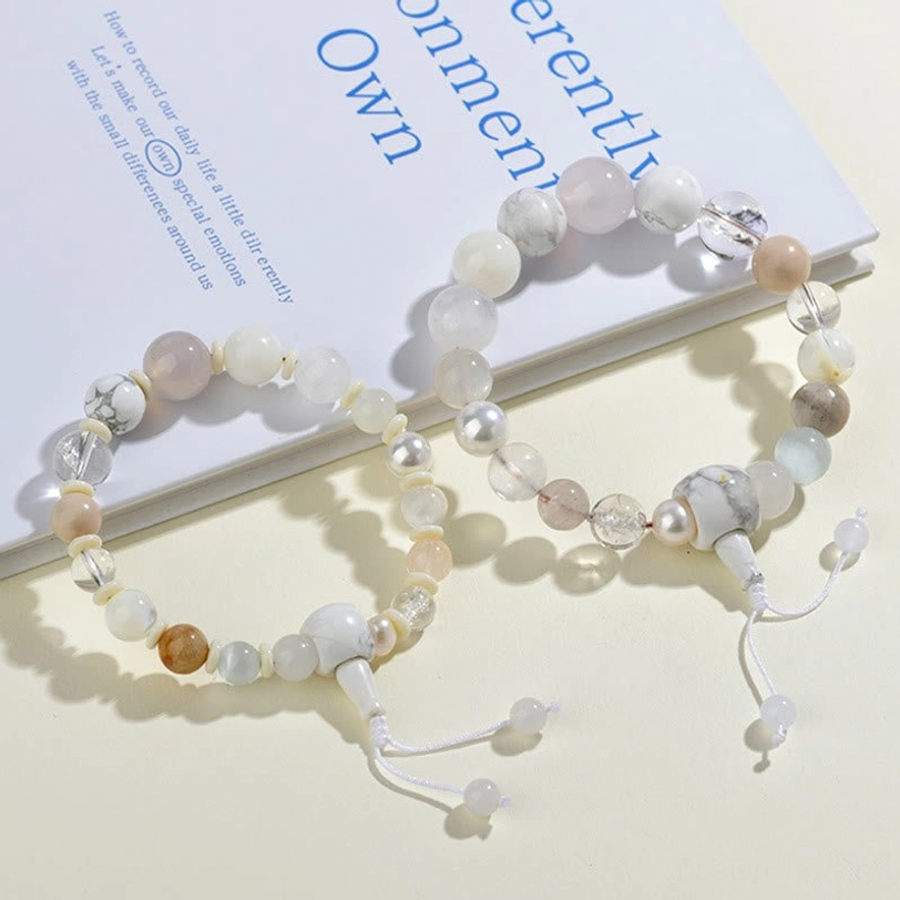 Two matching white agate pearl bracelets - overhead flat lay on printed book page showing paired natural stone beads with matching tassel clasps