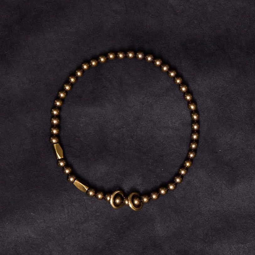 Tibetan brass couple bracelet with uniform antique bronze round beads and secure metal clasp on dark fabric