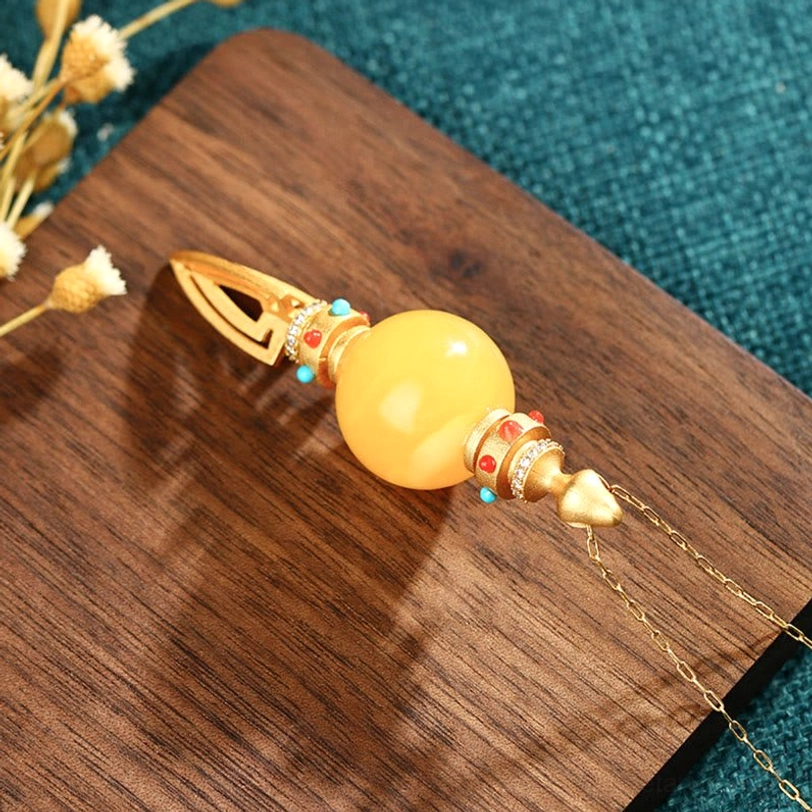 Flat lay of amber vajra necklace with chain on wooden surface, showing hollow vajra end detail and teal fabric