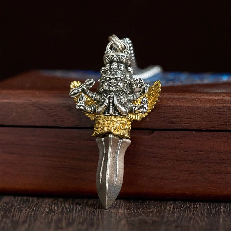 Close-up front view of Three Heads Six Arms Vajra pendant with gold carved base, silver deity figure with golden wings and sharp dagger tip