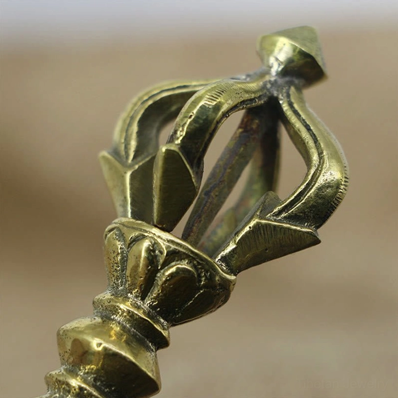 Close-up detail of five-prong vajra dorje crown top section in brassy gold copper, showing carved ritual base and symmetrical prong design on light background