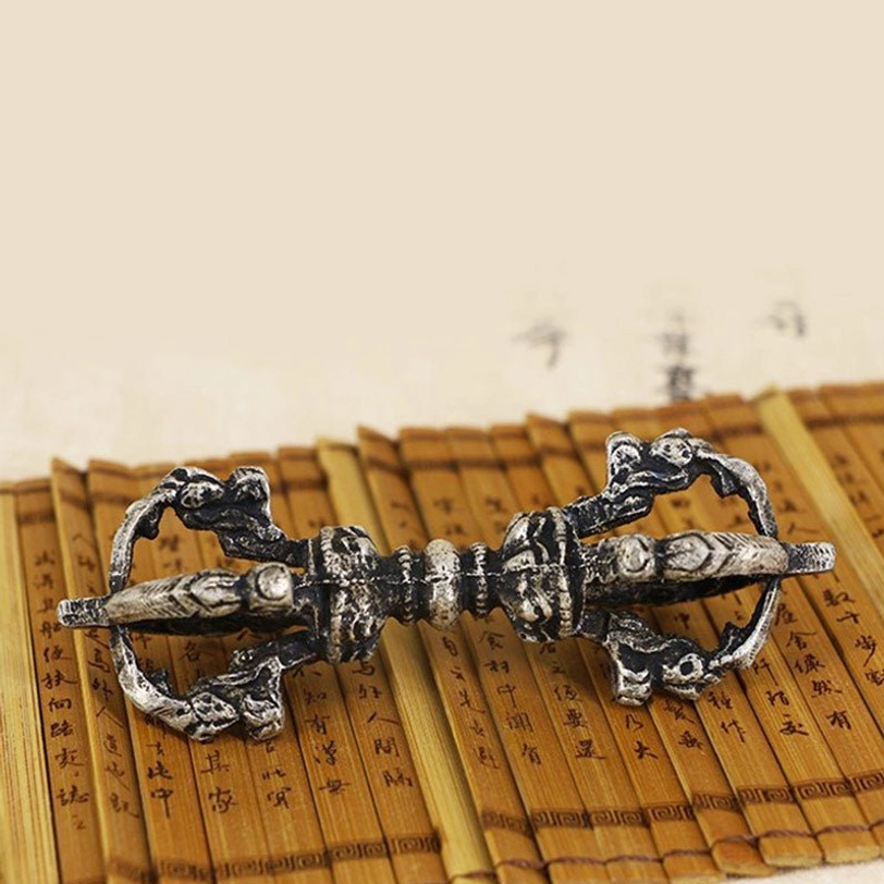 Single vajra dorje close-up top-down view showing intricate religious carvings and aged silver-black oxidation tone on bamboo slip desktop