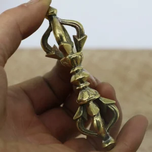 Handmade nepal copper vajra dorje held in hand, side view showing polished antique brass finish with symmetrical five-prong design and intricate ritual base