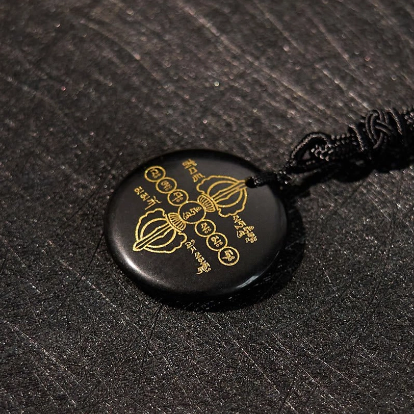Overhead side view of Tibetan Vajra Dorje black obsidian pendant with golden patterns on dark textured desktop background
