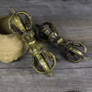 Two handcrafted Nepali five-prong vajra dorje copper ritual objects with aged bronze patina, photographed from overhead on weathered wooden surface with Buddha ceramic vessel, showing symmetrical religious embossments