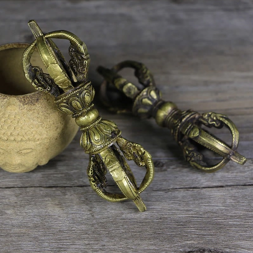 Two handcrafted Nepali five-prong vajra dorje copper ritual objects with aged bronze patina, photographed from overhead on weathered wooden surface with Buddha ceramic vessel, showing symmetrical religious embossments
