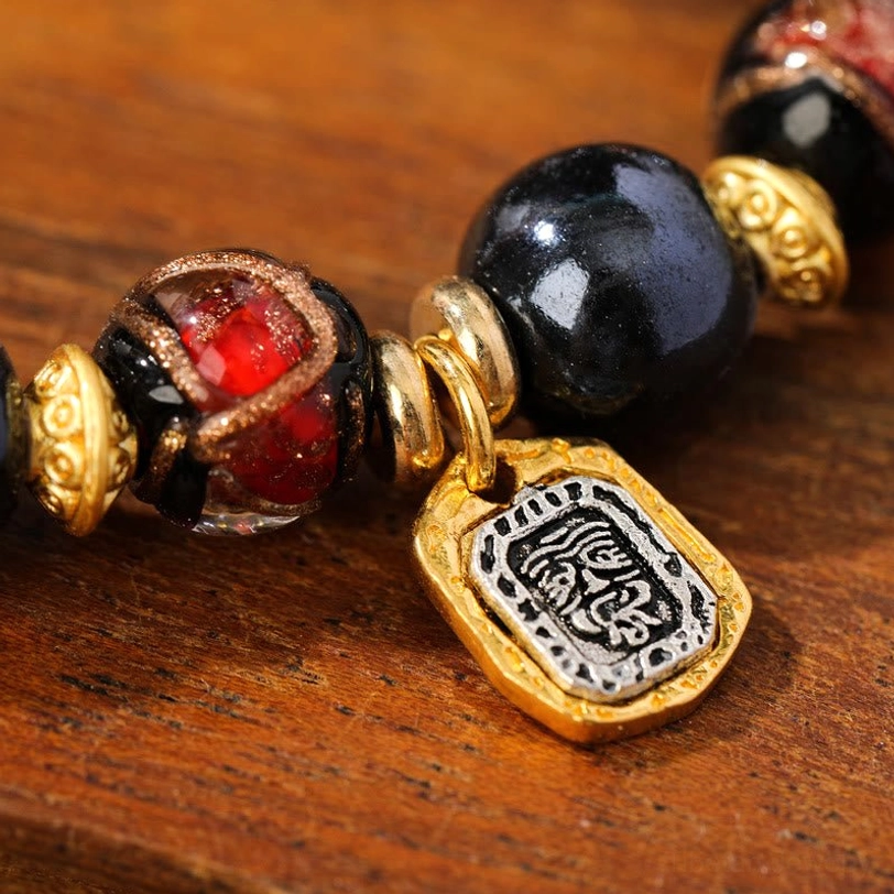 Tibetan wealth bracelet bead charm extreme close-up showing red glazed liuli glass and engraved metal pendant