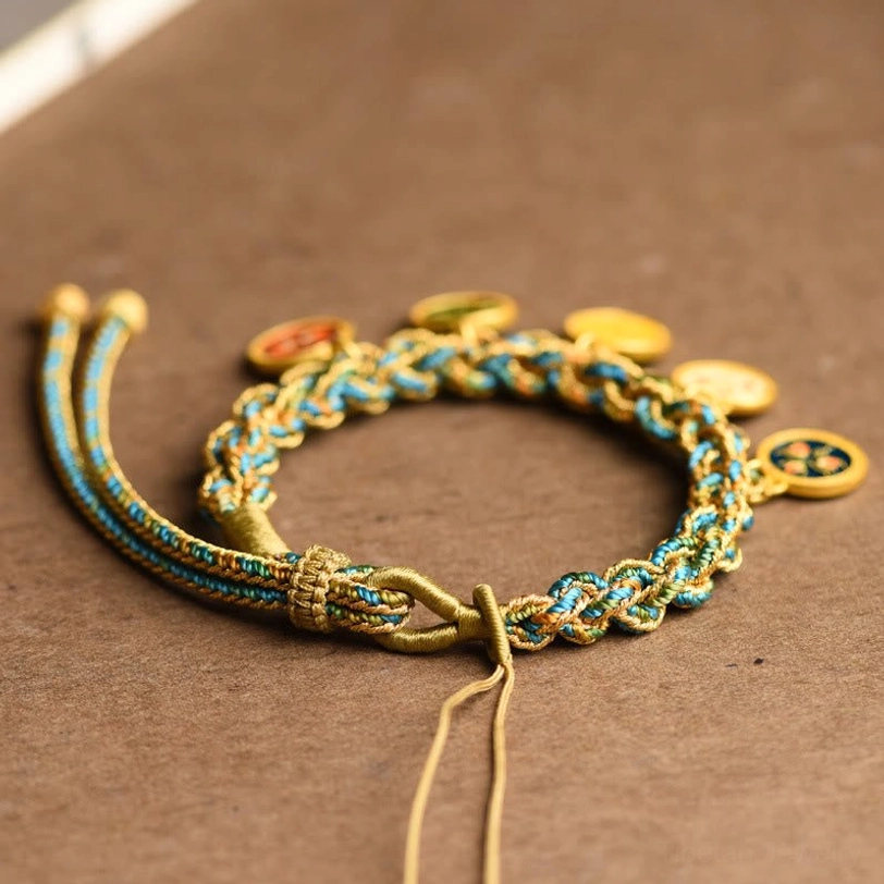 Close-up of Tibetan braided charm bracelet showing pull-tab adjustable clasp and mixed metal weave on wooden background