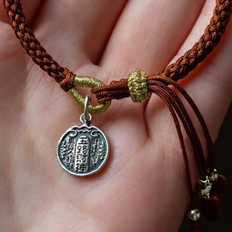 Tibetan prosperity bracelet with silver wealth pendant and red tassel held in palm, demonstrating charm size and beaded details