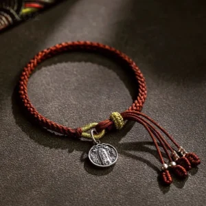 Handmade tibetan prosperity bracelet with engraved silver pendant and red tassel, close-up flat lay showing full bracelet design