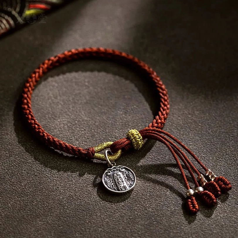 Handmade tibetan prosperity bracelet with engraved silver pendant and red tassel, close-up flat lay showing full bracelet design