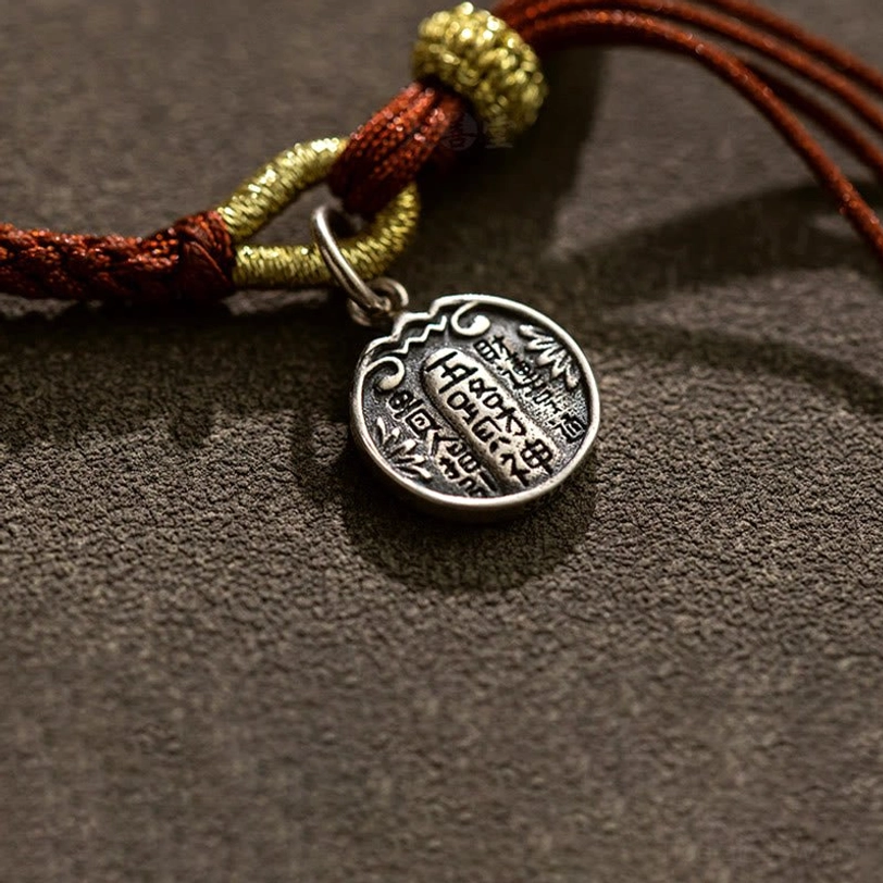 Close-up macro detail of sterling silver five directions wealth god pendant with engraved chinese characters and braided knots