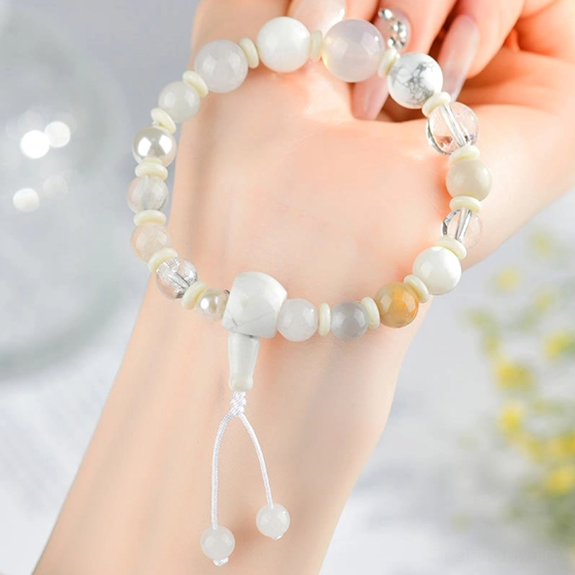 White agate pearl bracelet worn on wrist - first-person view with soft floral background showing natural stone beads and tassel