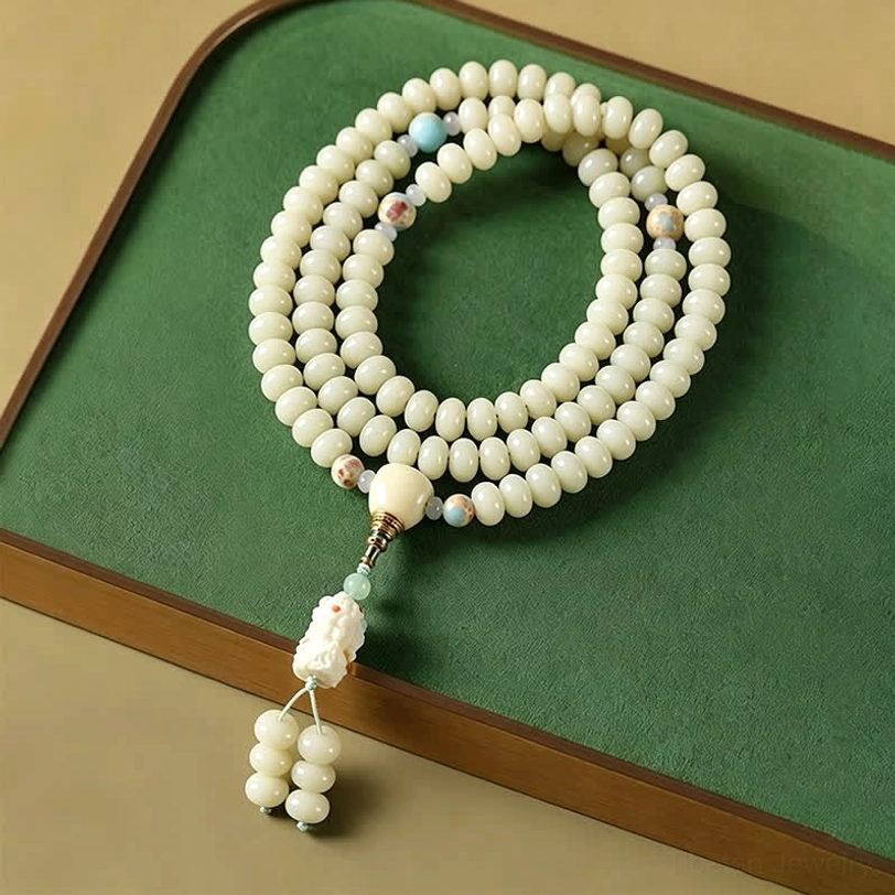 White bodhi seed 108 bead mala displayed on green tray with carved pendant tassel, overhead flat lay view