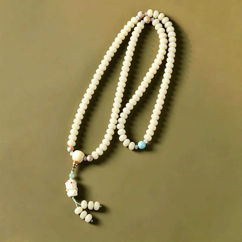 Long strand white bodhi seed mala with blue spacer bead and carved tassel pendant on muted green background