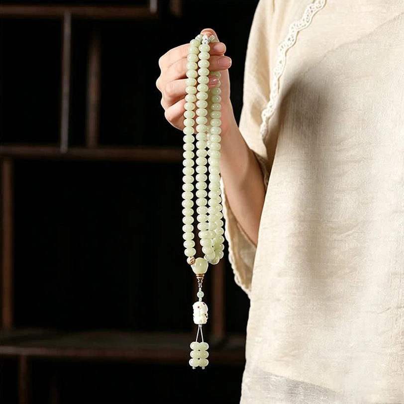 Hand-woven white bodhi seed mala draped over palm showing carved tassel pendant detail