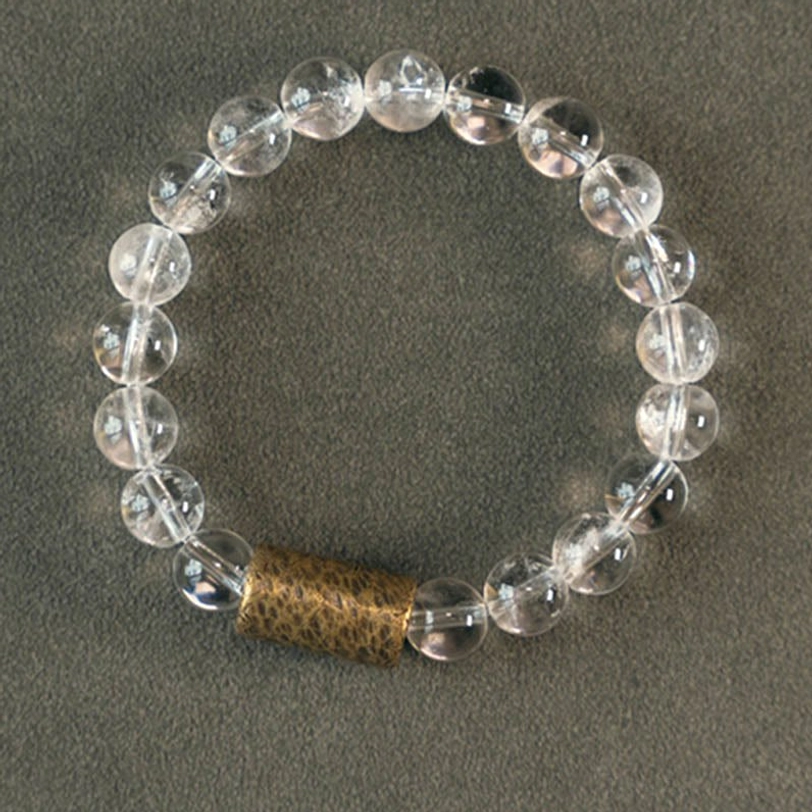Natural crystal healing bracelet with uniform clear quartz beads and textured copper spacer on grey fabric background