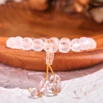 White crystal frosted quartz meditation bracelet with golden tassel pendant displayed on wooden surface