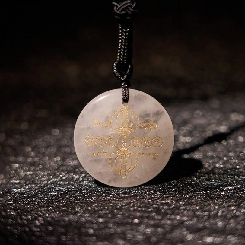 Close-up front view of pale clear crystal Vajra Dorje pendant with golden Buddhist engravings on glittery dark background