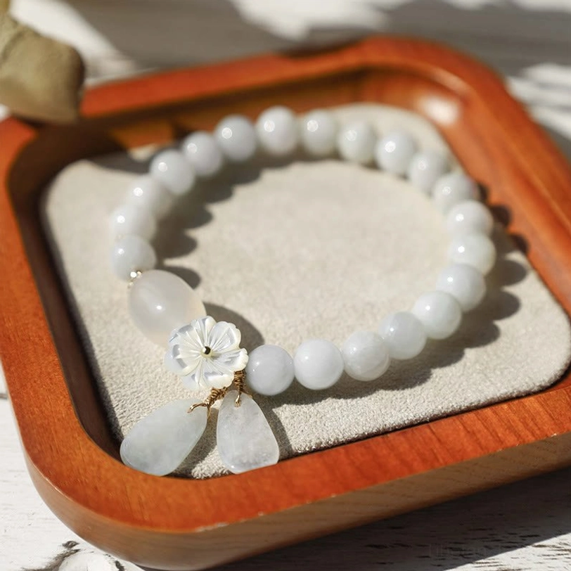 White jade beaded bracelet with shell flower charm and teardrop stone accents on velvet-lined wooden tray