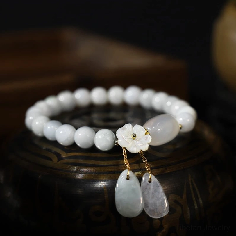 White jade beaded bracelet with oval jade bead, shell flower, and dual teardrop charms on carved wooden display