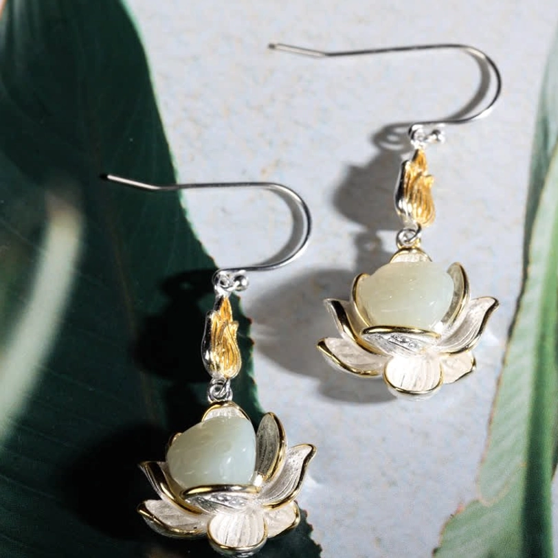 White jade lotus drop earrings arranged on bamboo mat with linen fabric and lotus pod design detail