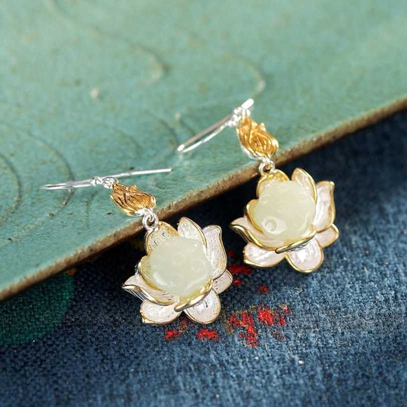 White jade lotus drop earrings flat lay on embroidered fabric showing shiny gold accents and silver lotus petal edges