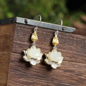 White jade lotus drop earrings on wooden display stand with gold and silver dual-tone metal accents