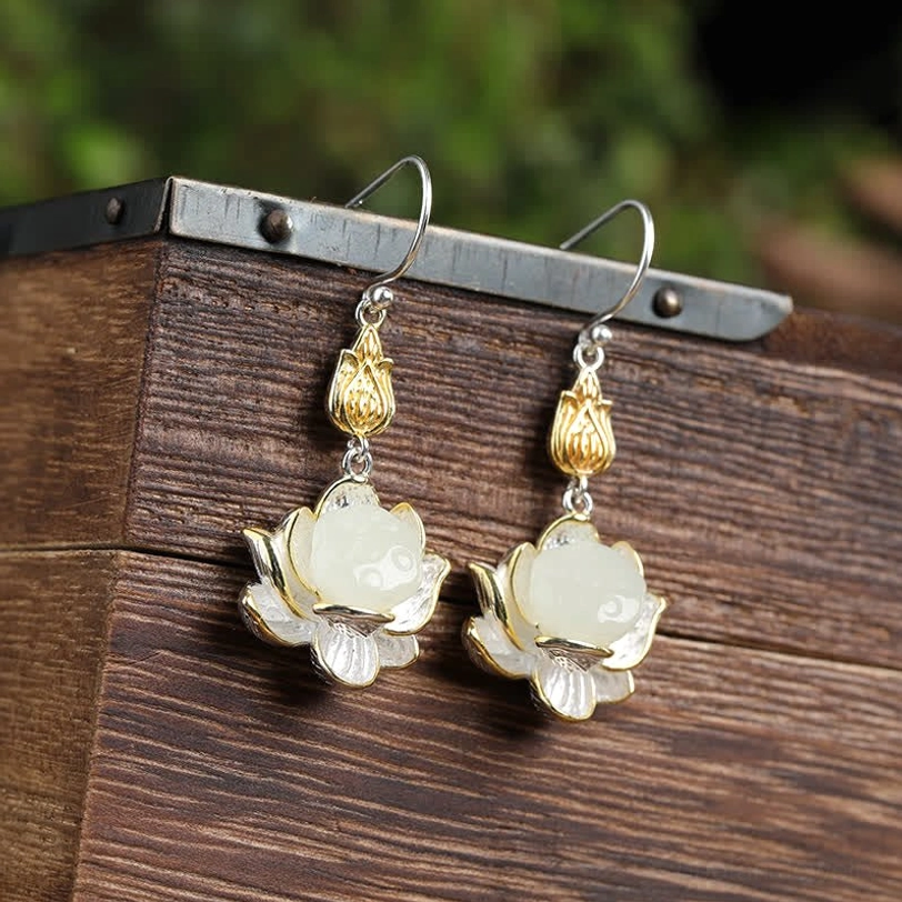 White jade lotus drop earrings on wooden display stand with gold and silver dual-tone metal accents