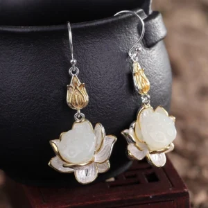 Close-up of white jade lotus drop earrings hanging on ceramic pot showing silver ear hooks and intricate lotus petal details