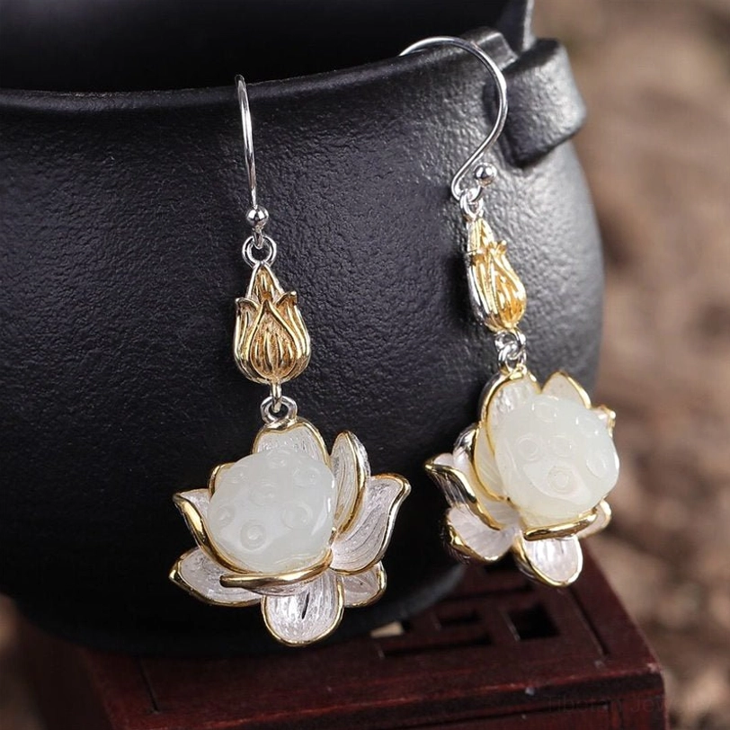 Close-up of white jade lotus drop earrings hanging on ceramic pot showing silver ear hooks and intricate lotus petal details