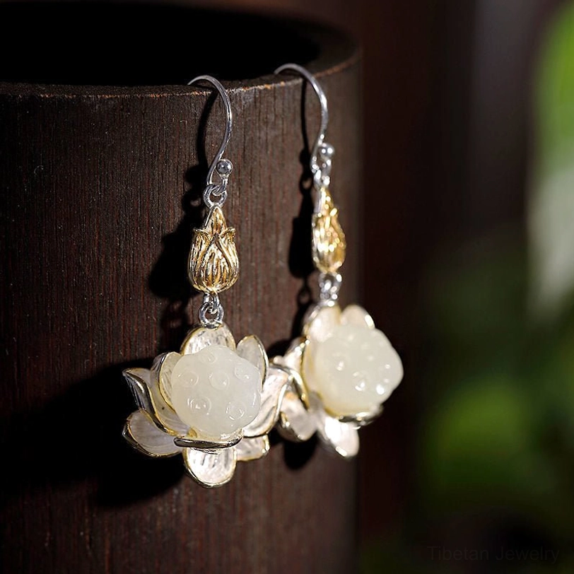 White jade lotus drop earrings displayed on dark wood with two-tone gold and silver metal settings