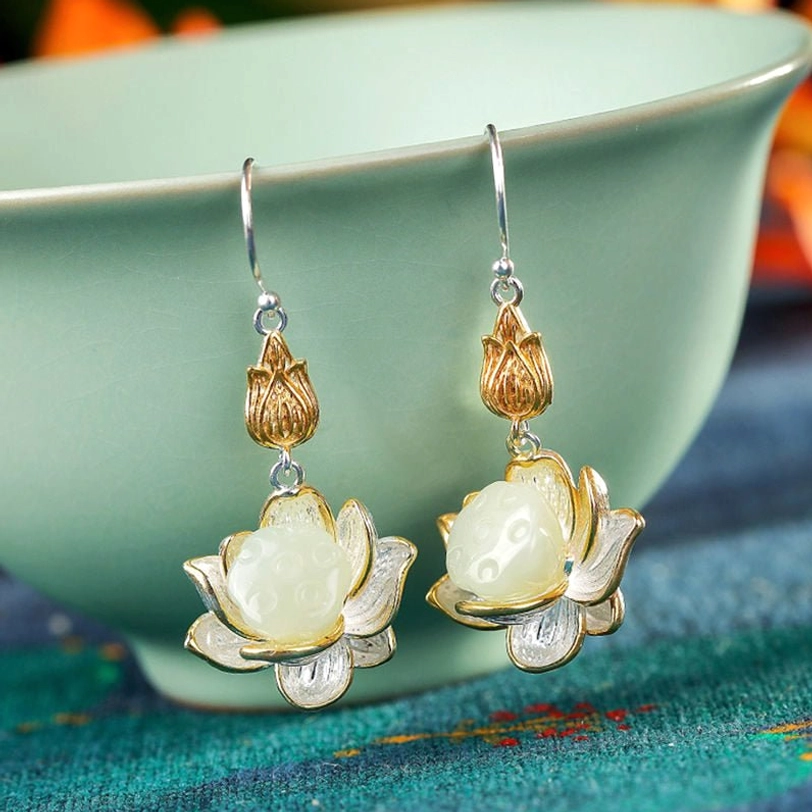 White jade lotus drop earrings pair in soft lighting on green porcelain bowl with embroidered cloth background