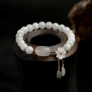 White jade protection bracelet with shell flower charm and teardrop stone pendants on dark wooden display stand