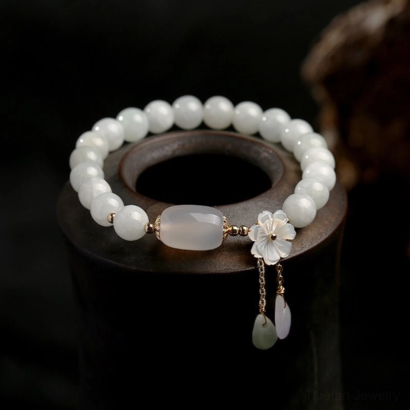 White jade protection bracelet with shell flower charm and teardrop stone pendants on dark wooden display stand