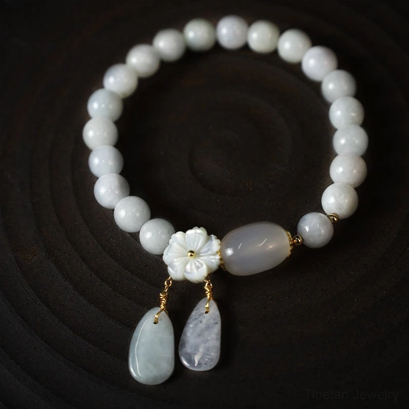 Round white jade beaded bracelet with oval jade accent, shell flower, and teardrop pendants on dark circular stand