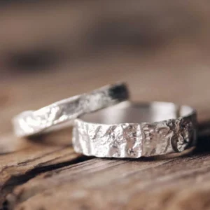 Wide matte silver hammered band couple rings on rustic wood - matching set close-up
