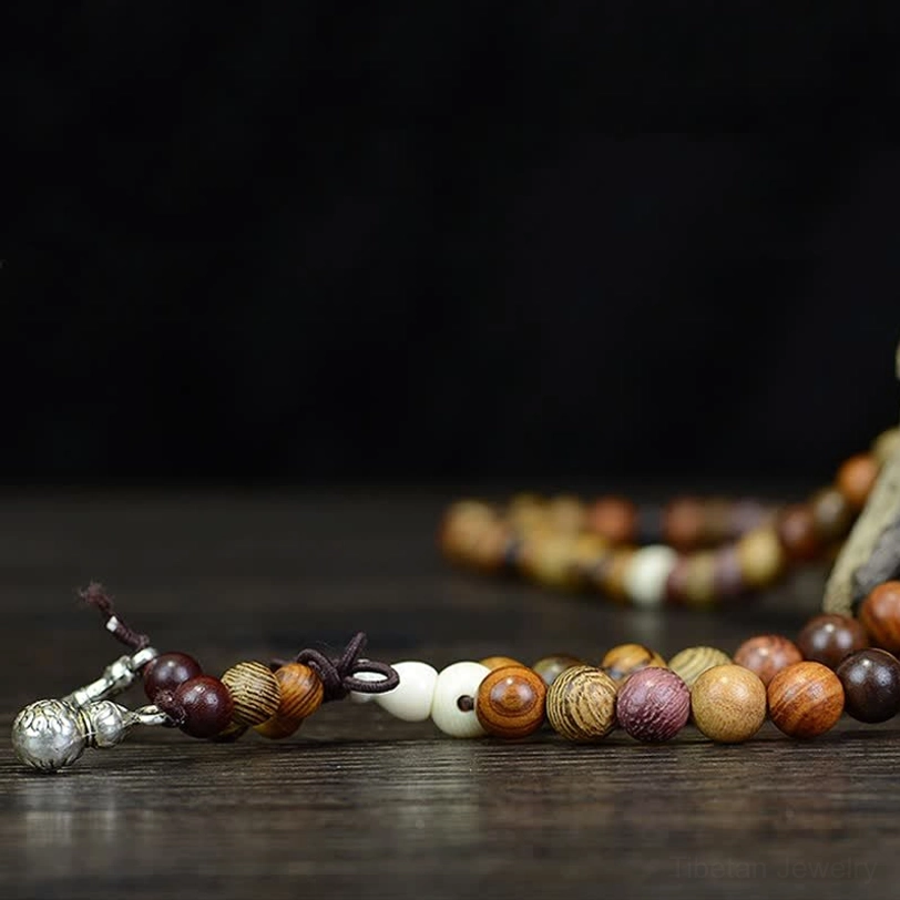 Natural wood prayer mala strand side view on dark wooden table with mixed brown beads and silver charms