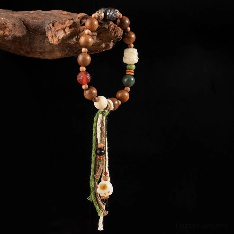 Tibetan protection bracelet with brown wooden beads, green and red accent beads, and carved black spacer detail on light beige background
