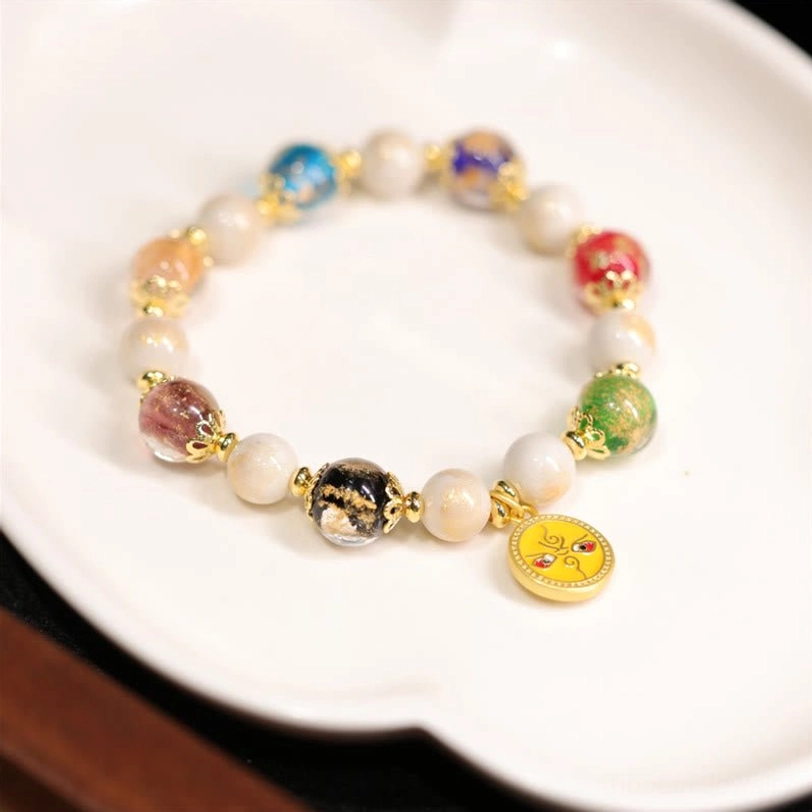 Yellow God of Wealth Tibetan bracelet featuring yellow enamel pendant, white porcelain beads, and gold-toned metal accents on ceramic display