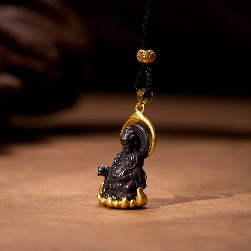 Yellow Jambhala Buddha necklace side profile view, displaying intricate details of the Buddha figure, gold lotus throne and halo, black cord with gold bead on wooden surface