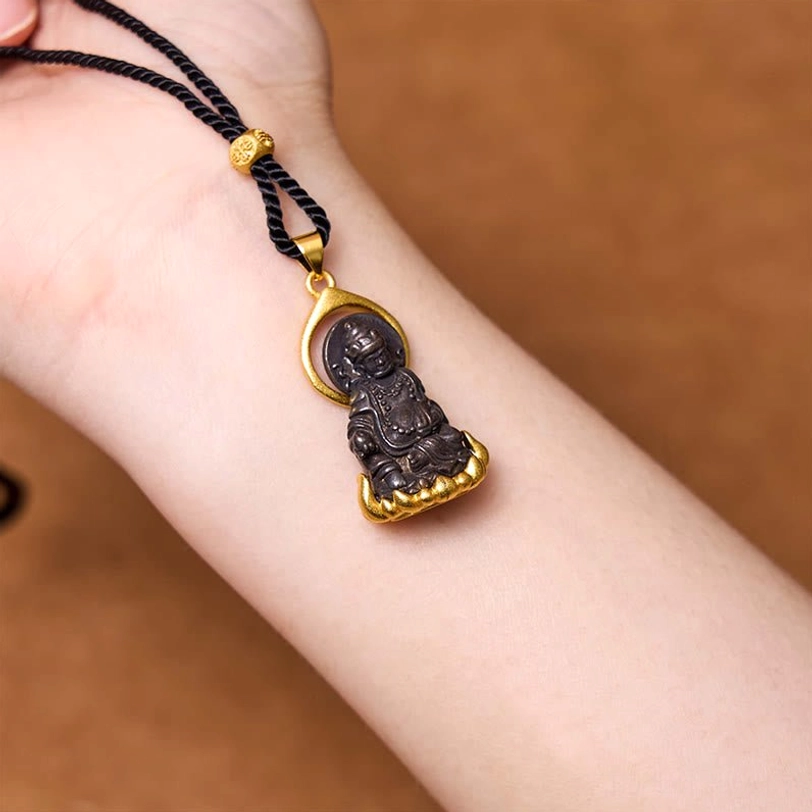 Tibetan Yellow Jambhala pendant worn on wrist, showing dual-tone design with seated Buddha figurine on golden lotus base and black braided cord with gold accent bead