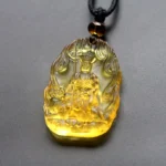 Yellow Ksitigarbha Buddha Liuli crystal pendant with flame carved border, seated Bodhisattva holding staff and lion symbol, black braided cord with amber bead accent