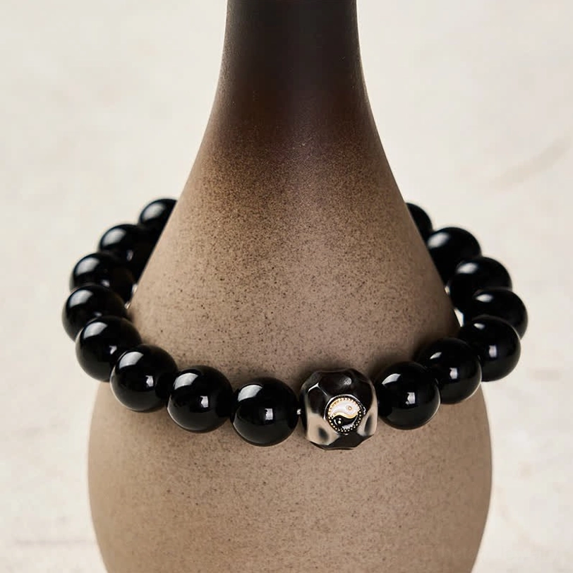 Yin Yang round bead bracelet with glossy black beads and charm on ceramic vase display